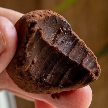 A hand holding a bitten chocolate truffle coated in cocoa powder, revealing the smooth, rich, dark chocolate filling inside—perfect for chocolate truffles lovers.