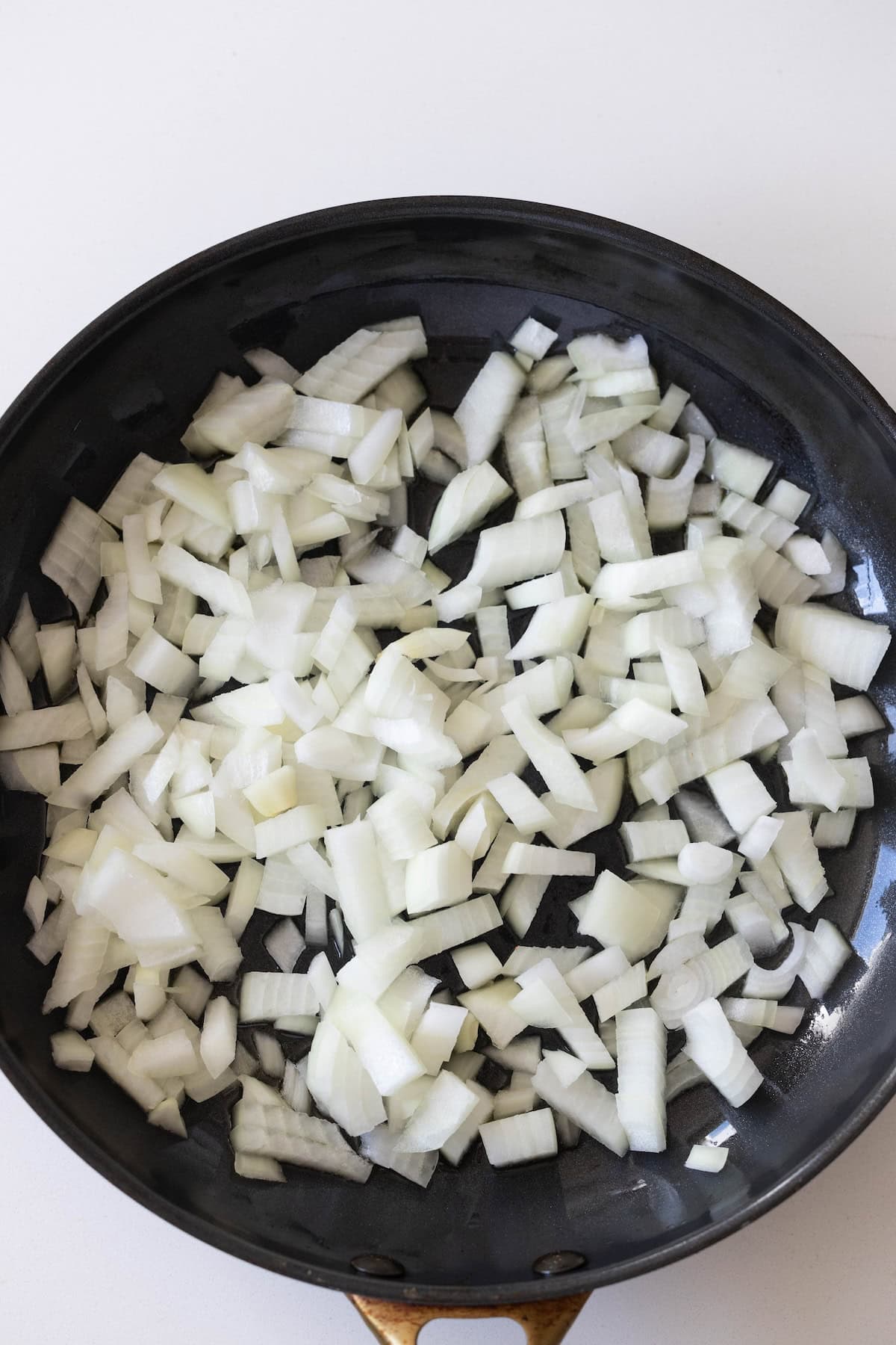 A frying pan filled with raw, chopped white onions and cabbage rests on a white surface, ready to be mixed with noodles.