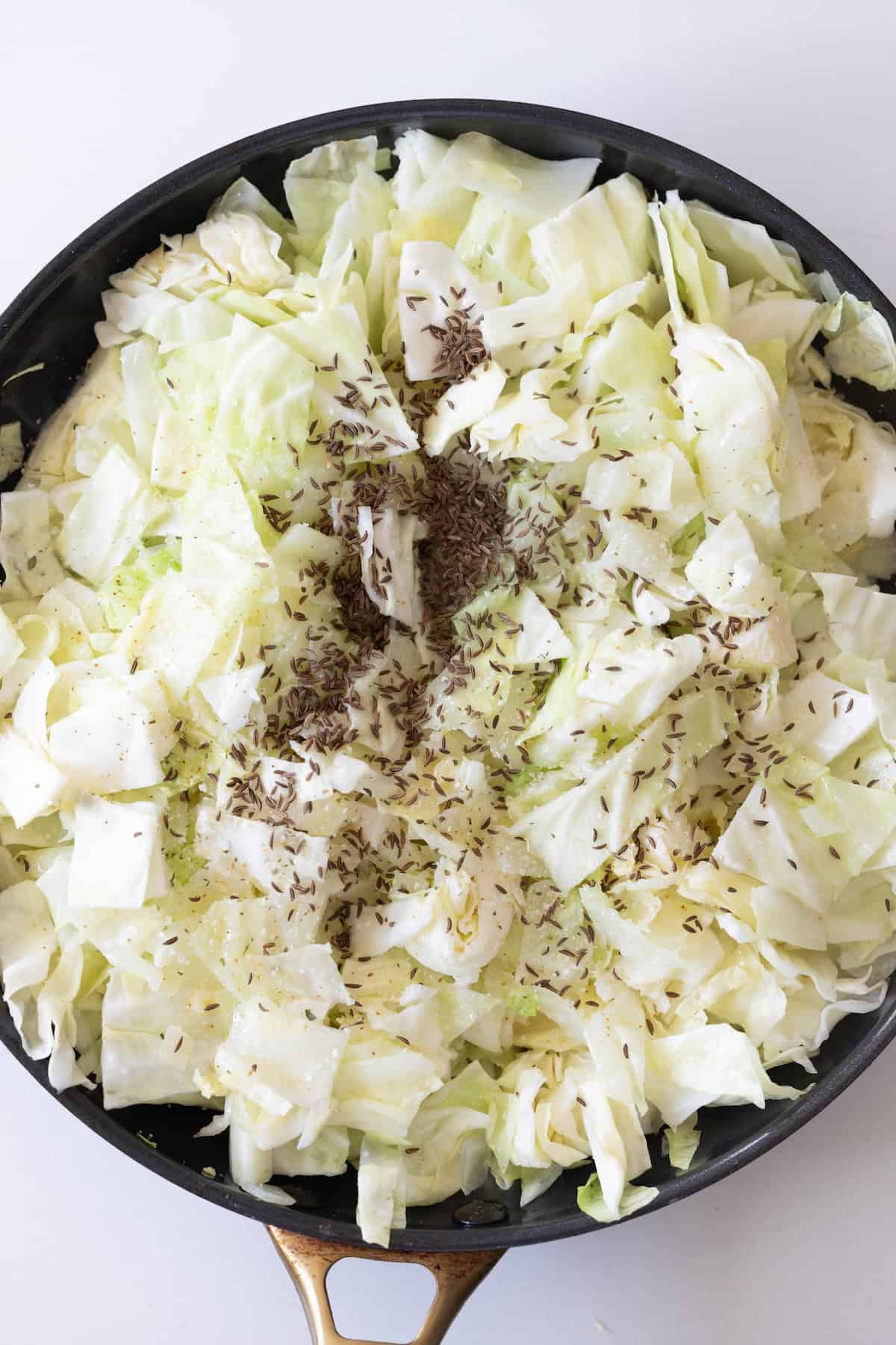 Chopped cabbage with caraway seeds and pepper in a black skillet, perfect for creating delicious Cabbage and Noodles.