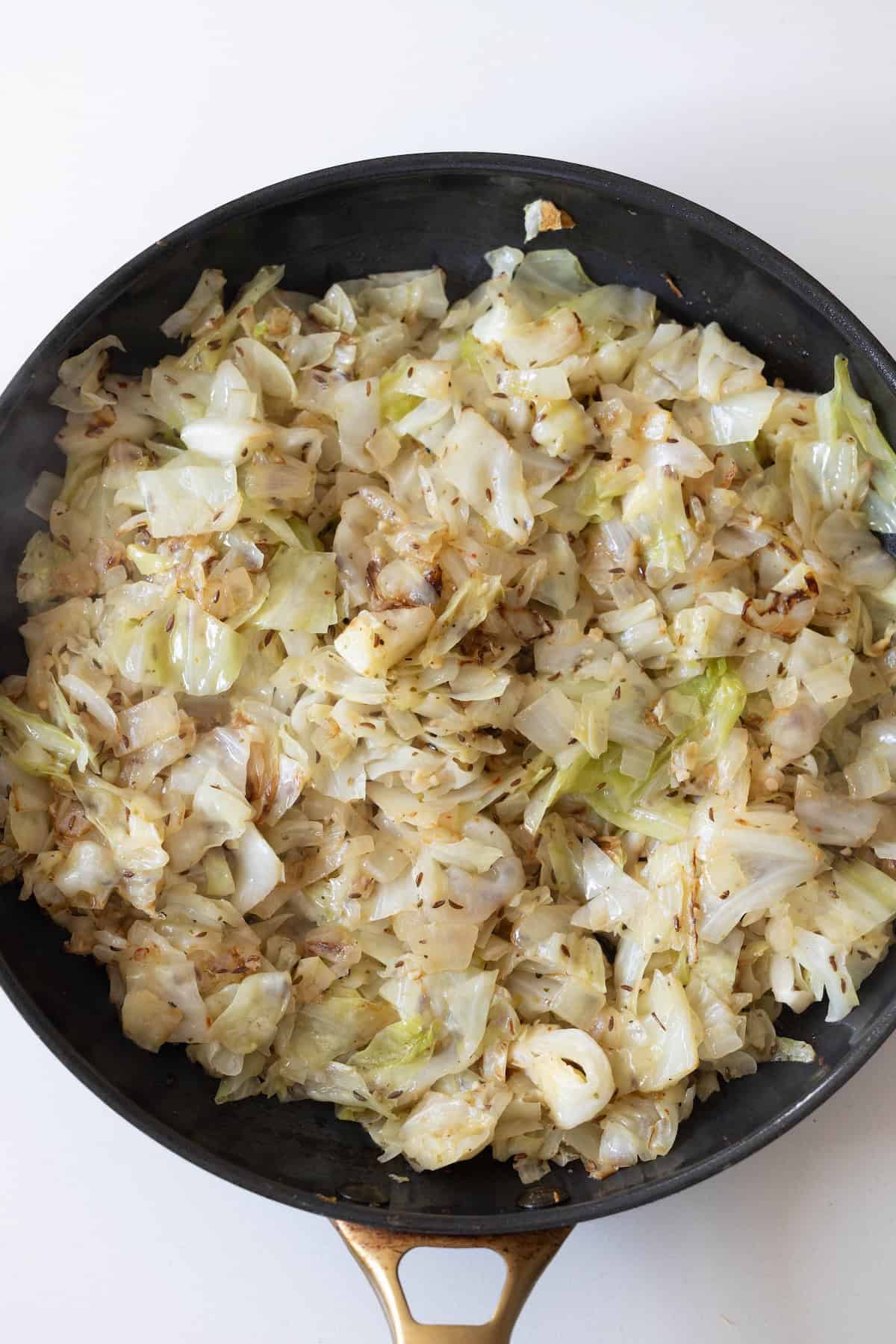 A black skillet filled with sautéed chopped cabbage and noodles, showing browned edges, rests on a white surface.