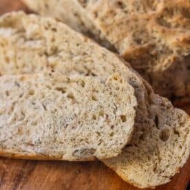 Two slices of flavorful dilly bread are displayed on a wooden cutting board, with the rest of the loaf visible in the background.