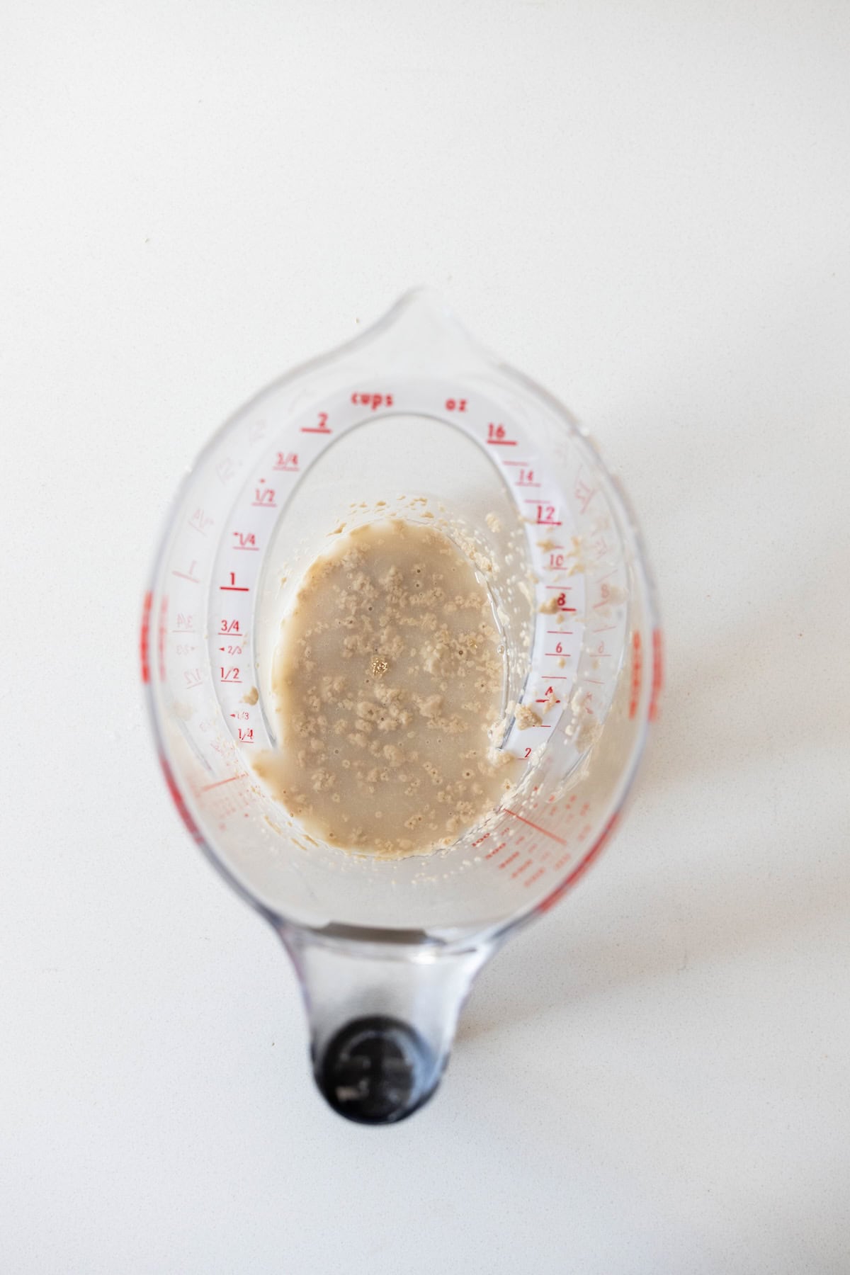 A glass measuring cup containing liquid and bubbles or granules sits on a white surface, viewed from above—an essential step in preparing a classic Dilly Bread Recipe.