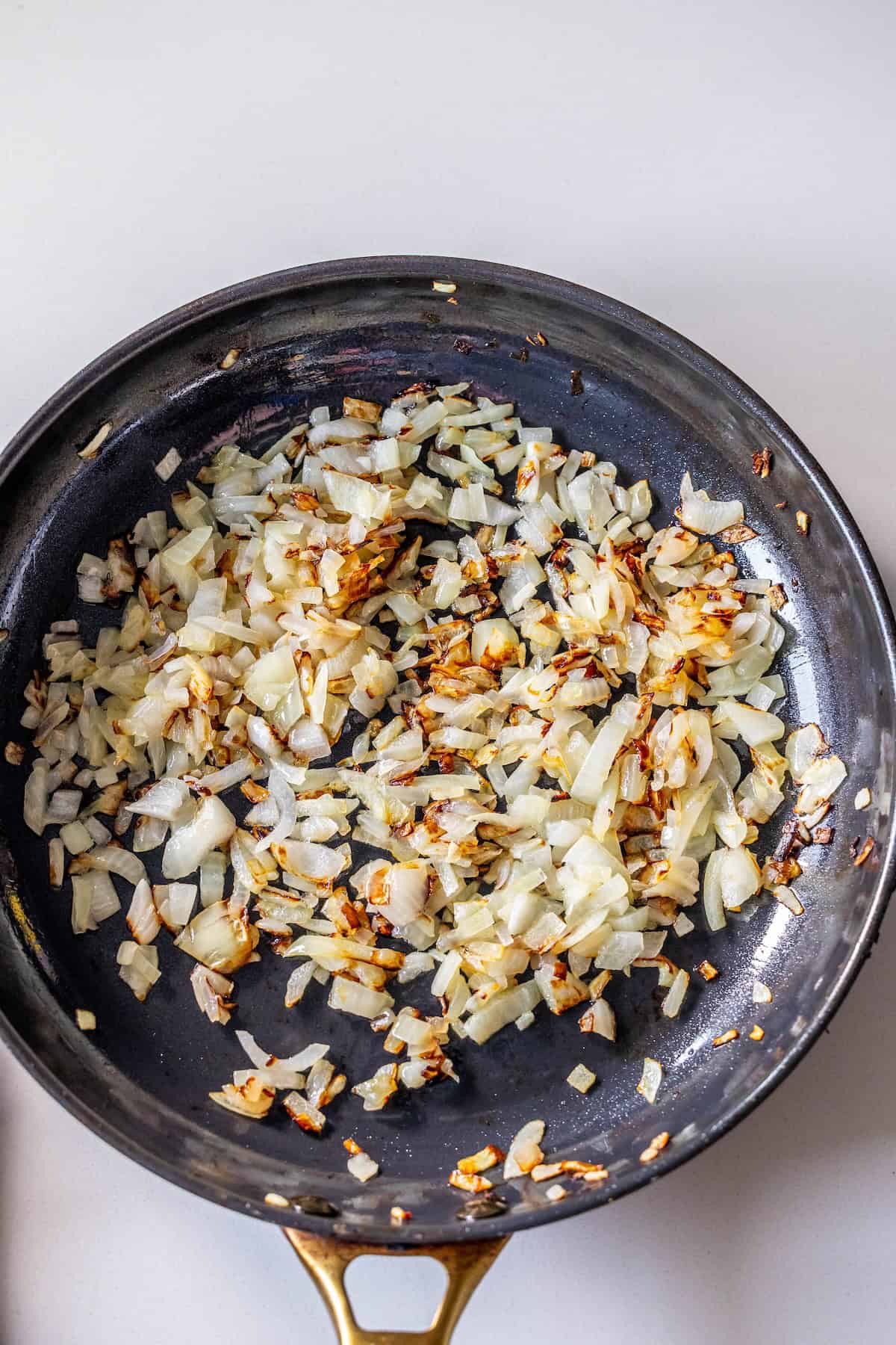 Chopped onions being sautéed in a black skillet with some pieces lightly browned, perfect as a savory base for a flavorful Brussels Sprouts Hash.