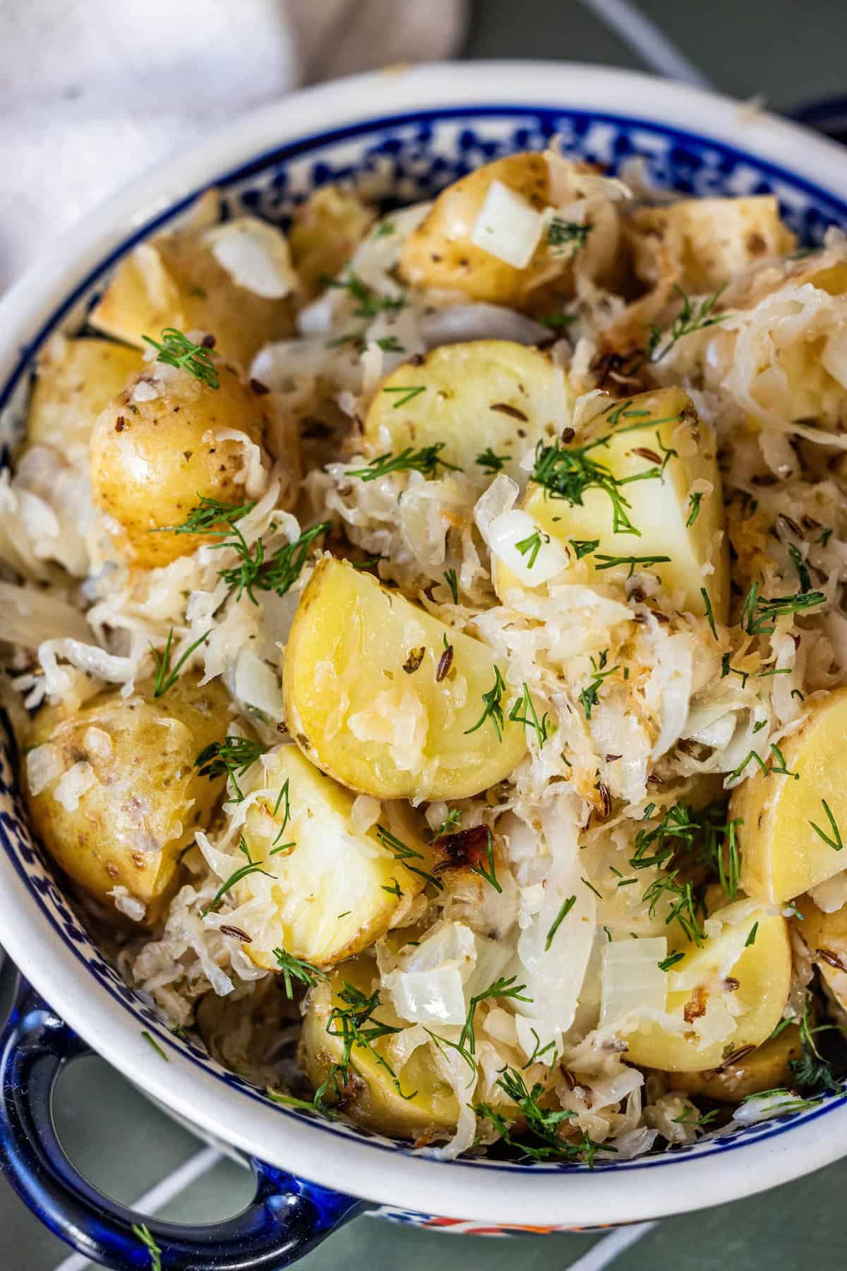 A bowl filled with roasted potatoes, sauerkraut, chopped onions, and fresh dill.