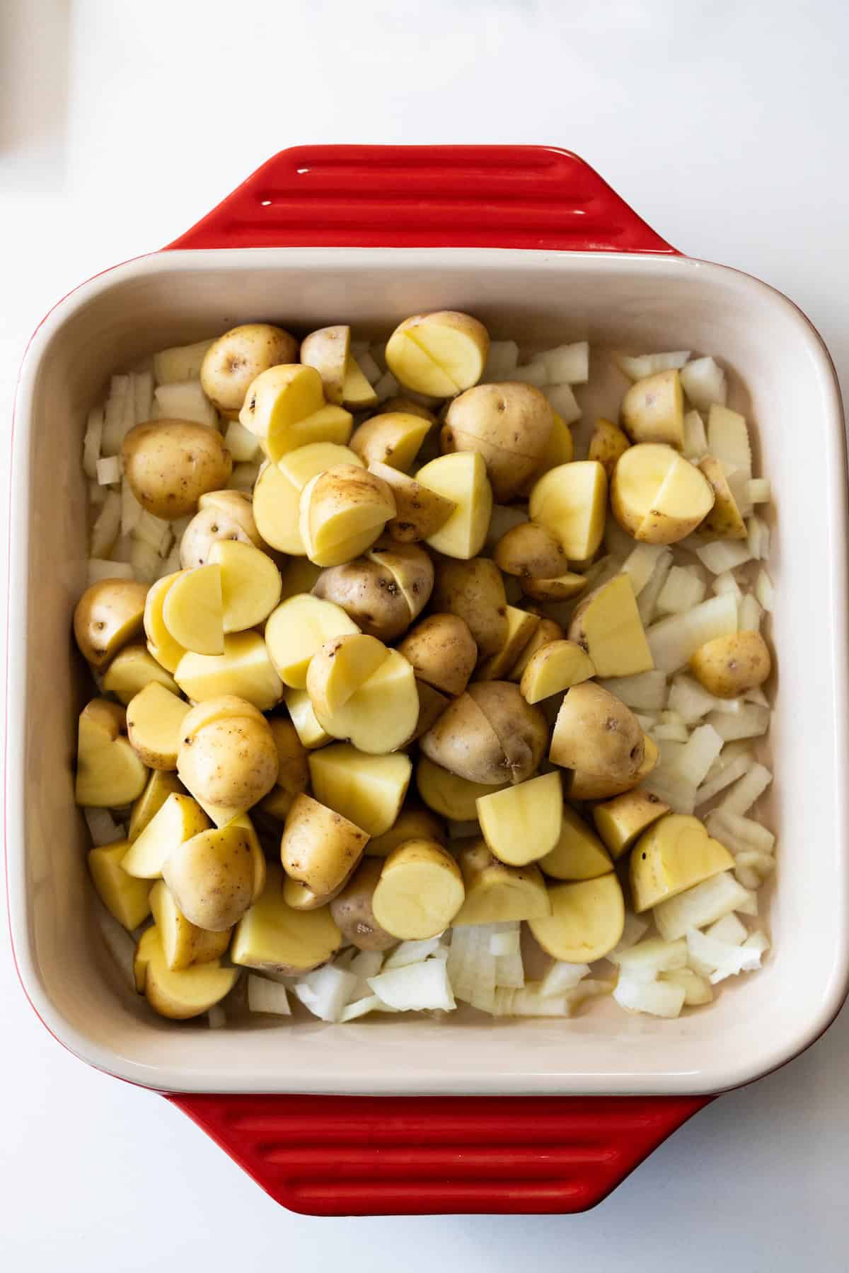 A baking dish with chopped onions, sauerkraut, and halved baby potatoes arranged on top, ready for roasting.