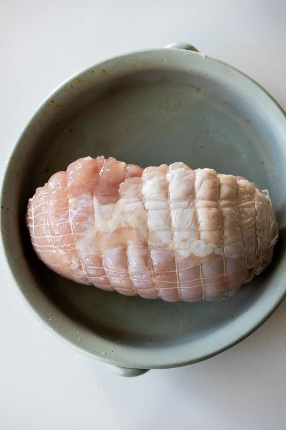A raw, netted pork roast sits in a round, light-colored ceramic dish—perfect for those who love roasting meats like air fryer turkey breast.