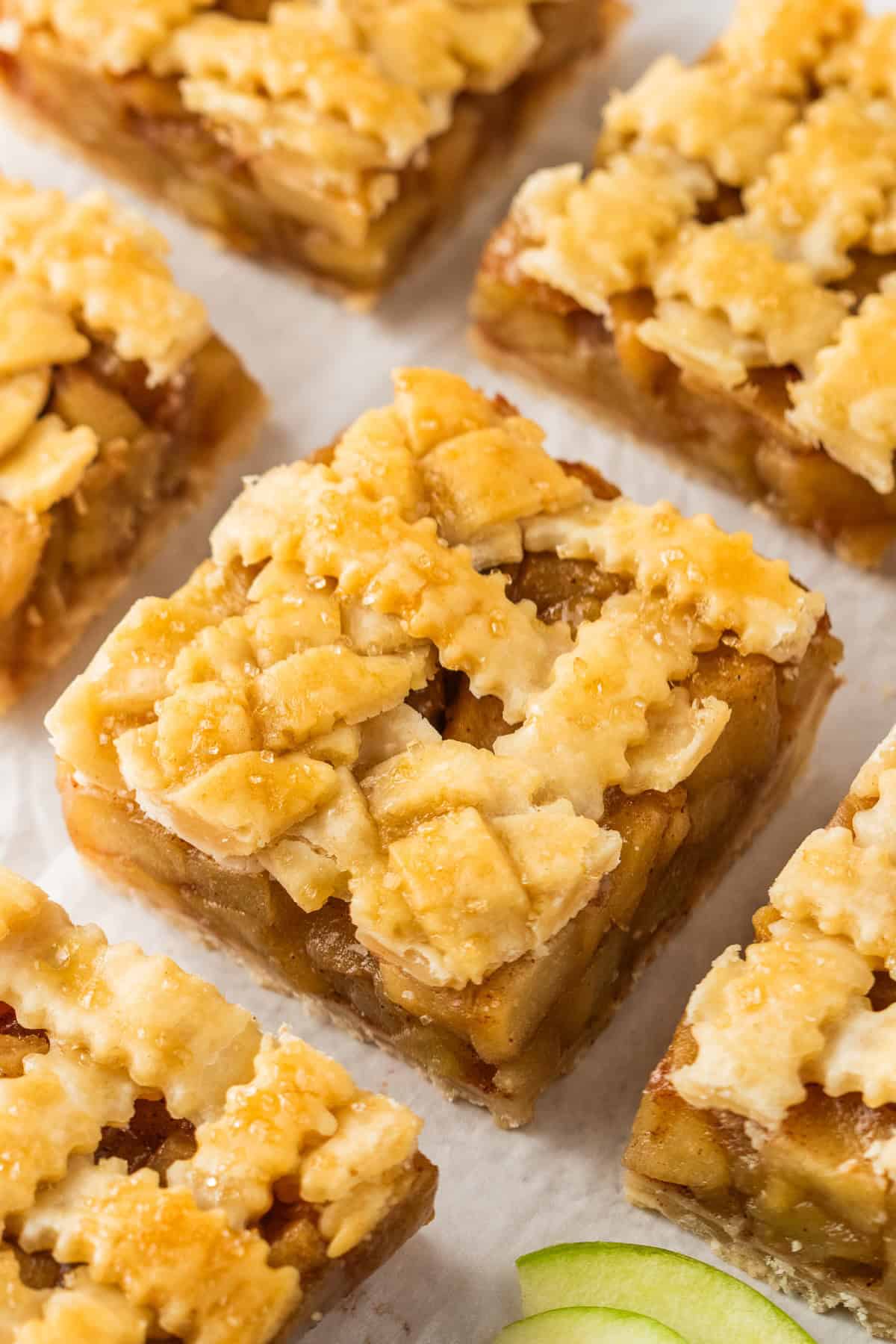 Close-up of several Apple Pie Bars with a lattice crust, arranged on parchment paper.