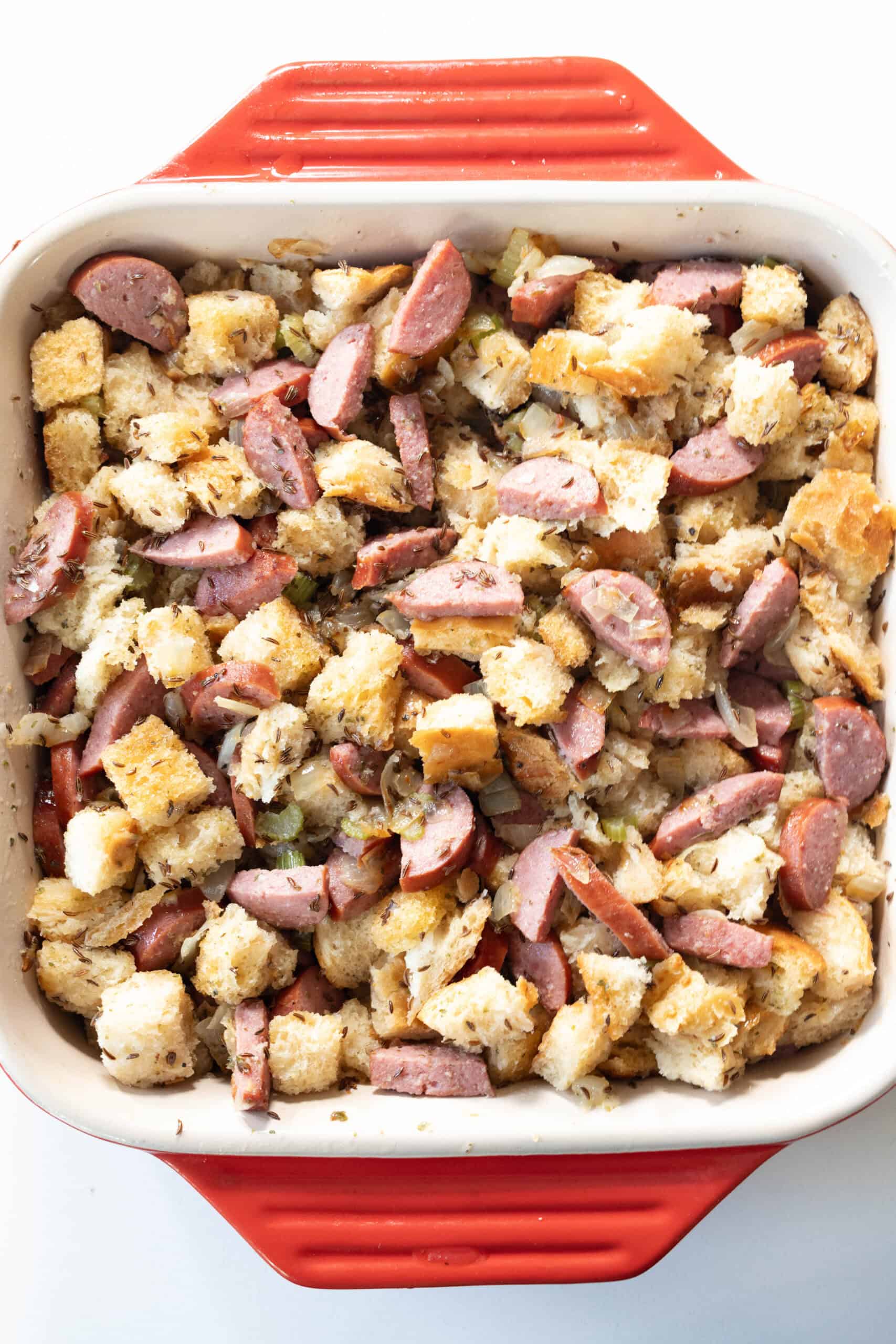 A square red baking dish filled with a mixture of cubed bread and sliced Polish Kielbasa baked together for a savory stuffing.