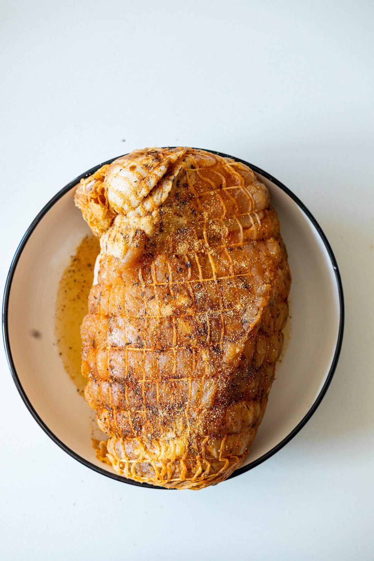 Seasoned and netted cajun turkey breast in a white bowl, ready for cooking on a white surface—perfect for preparing in your air fryer.