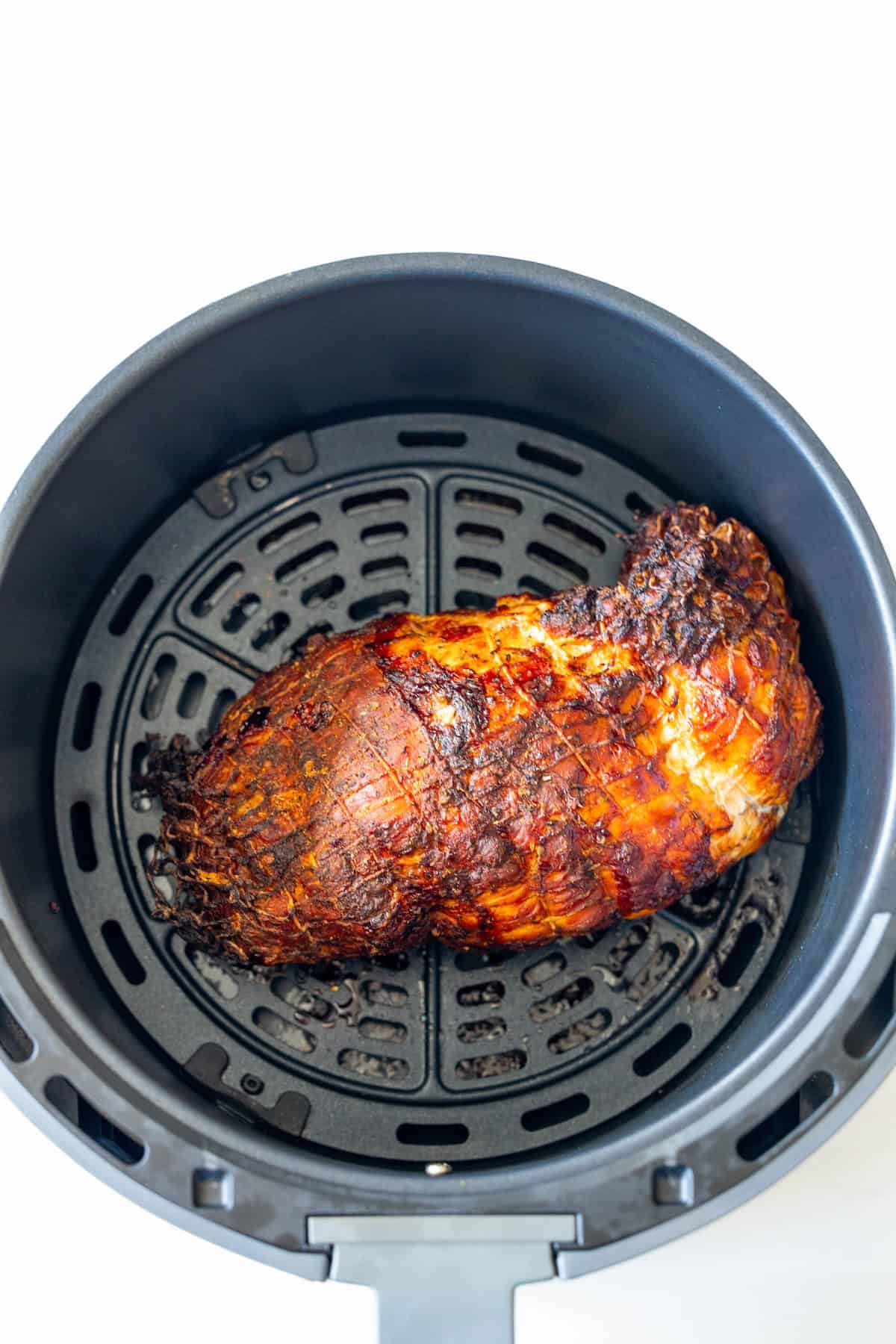 A cooked Cajun turkey breast sits inside the basket of an air fryer against a white background.