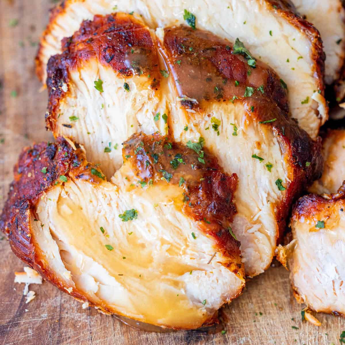 Sliced, cooked Cajun Turkey Breast with a browned, seasoned crust and sprinkled herbs on a wooden cutting board.