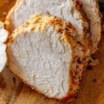 Close-up of several slices of seasoned Air Fryer Turkey Breast on a wooden cutting board.