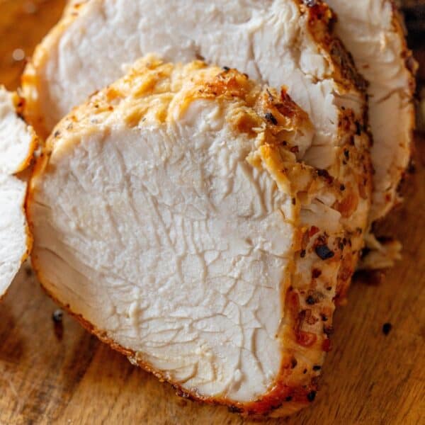 Close-up of several slices of seasoned Air Fryer Turkey Breast on a wooden cutting board.