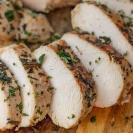 Sliced cooked chicken breast garnished with chopped herbs on a wooden cutting board—a presentation perfect for showcasing an Easy Turkey Recipe or Baked Turkey Tenderloin as well.