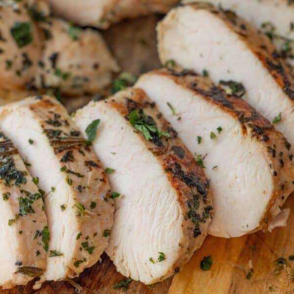 Sliced cooked chicken breast garnished with chopped herbs on a wooden cutting board—a presentation perfect for showcasing an Easy Turkey Recipe or Baked Turkey Tenderloin as well.