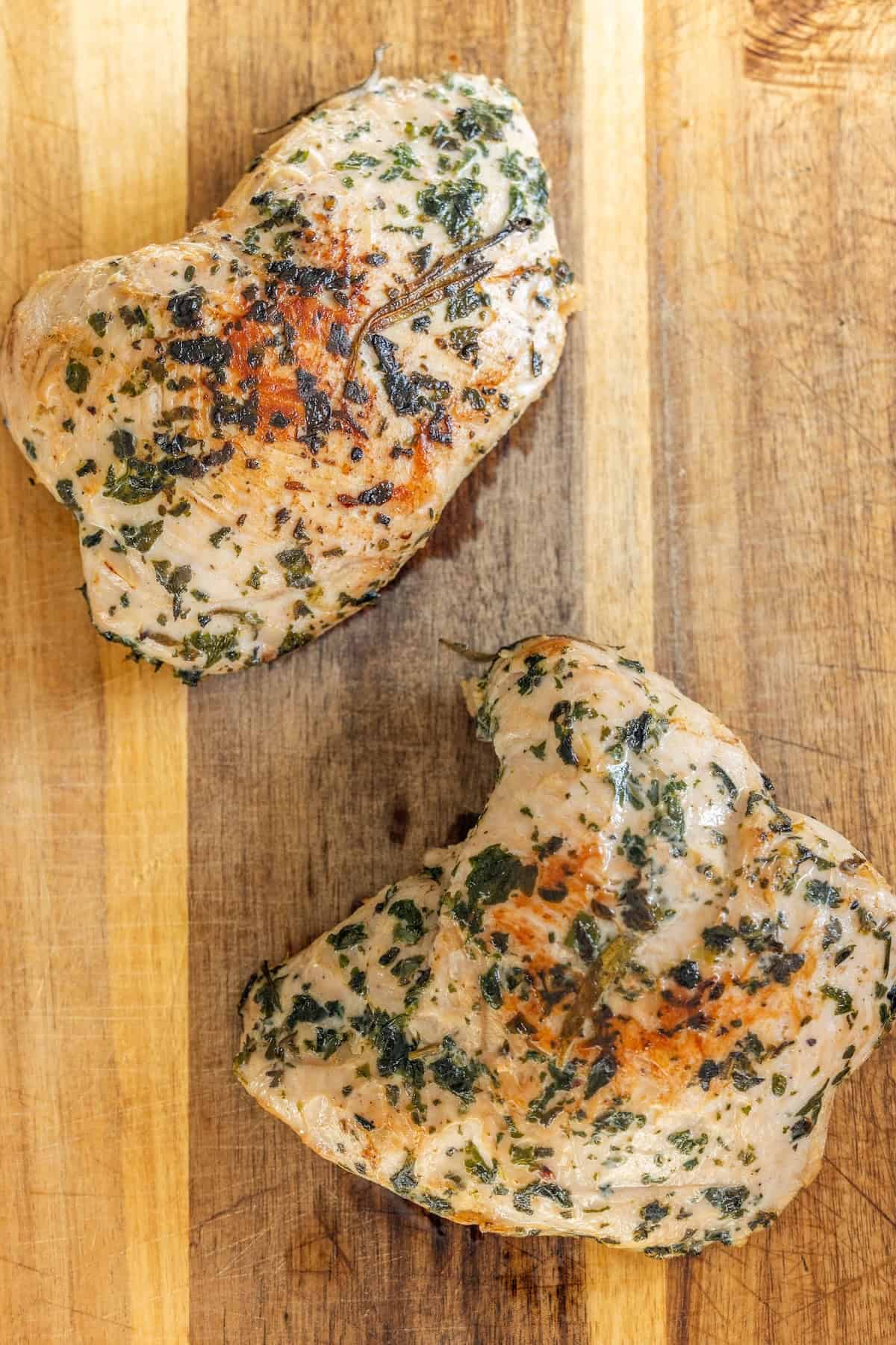 Two cooked, herb-seasoned turkey tenderloin pieces rest on a wooden cutting board—an easy turkey recipe perfect for any meal.