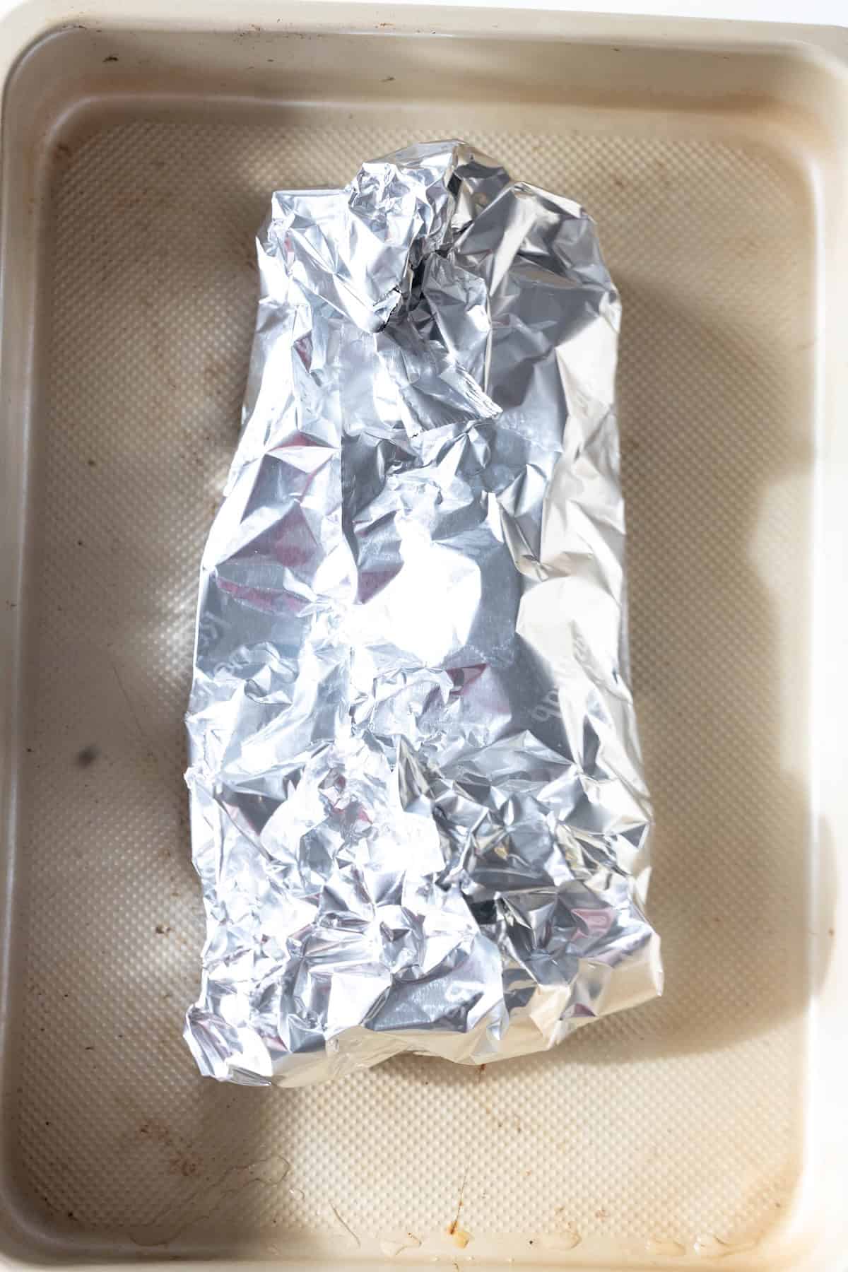 A baking tray with a rectangular object wrapped in crumpled aluminum foil, ready for an easy turkey recipe like baked turkey tenderloin.
