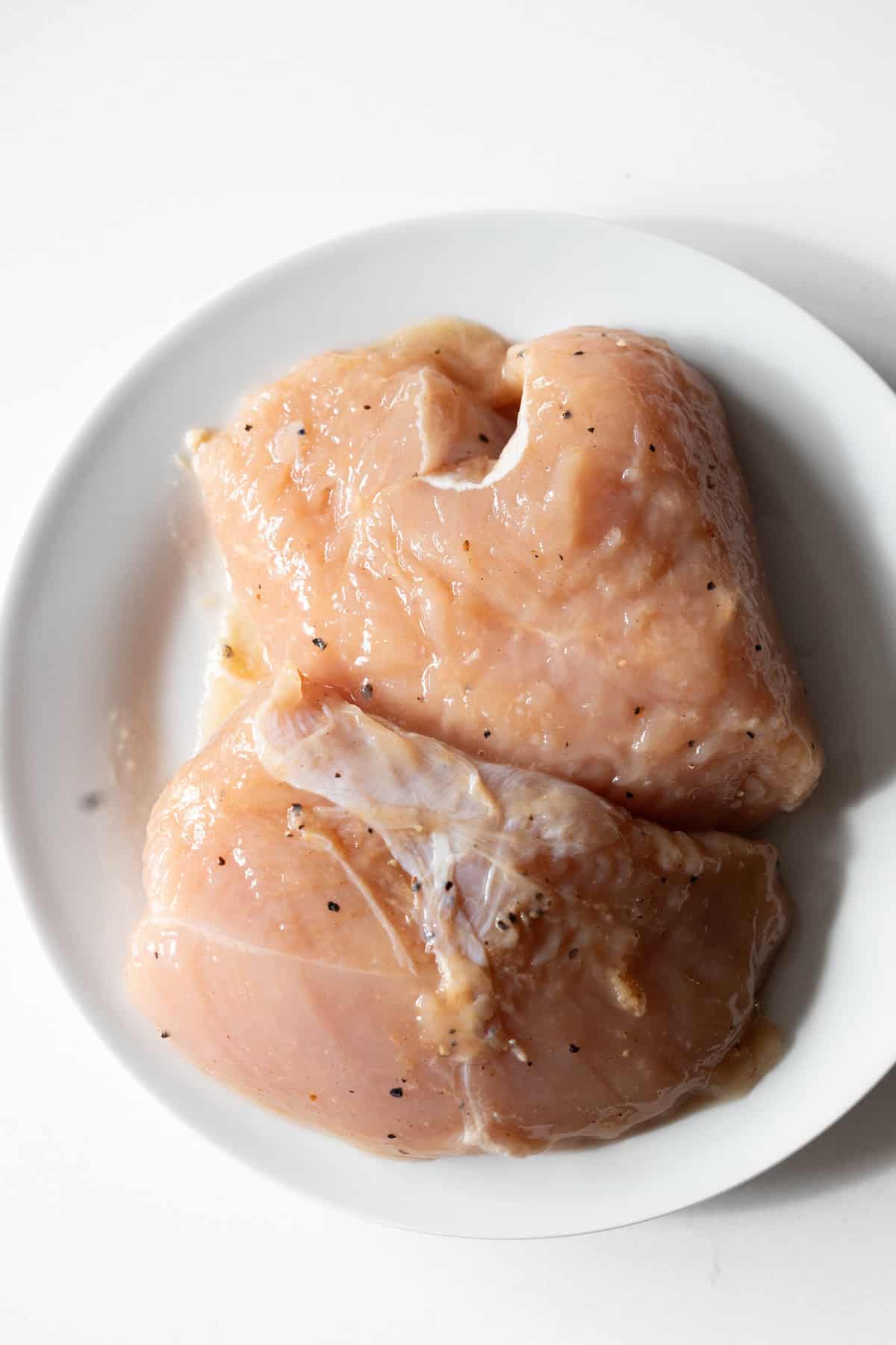 Two raw, seasoned turkey tenderloins are placed on a white plate against a white background—perfect for your next easy turkey recipe.