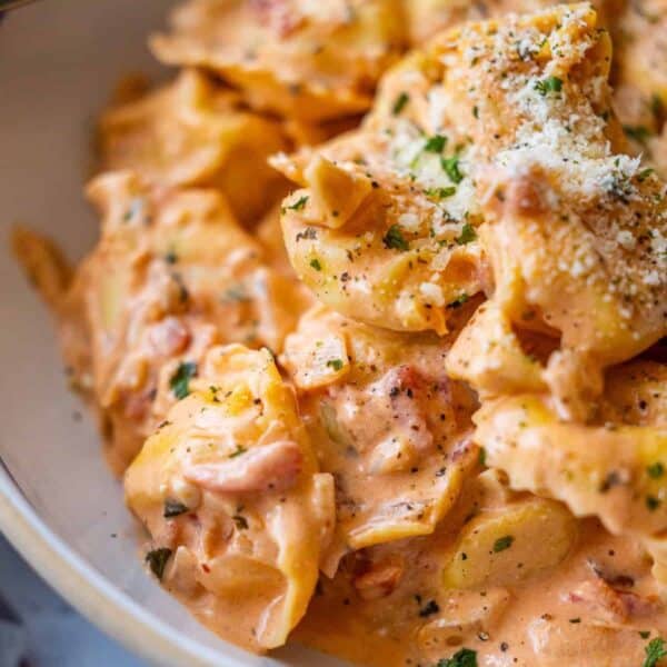 Close-up of creamy Marry Me Tortellini in a tomato-based sauce, garnished with chopped herbs and grated parmesan cheese.