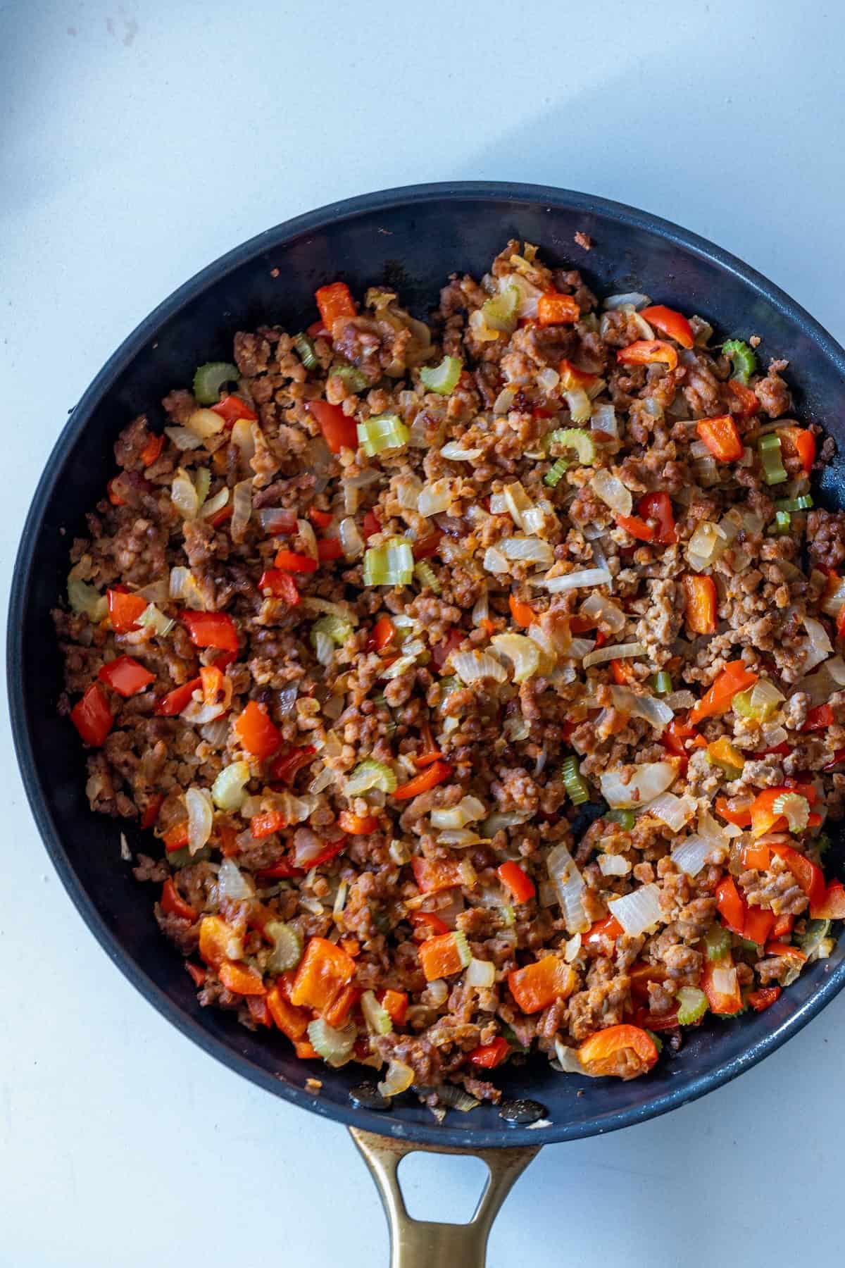 A bowl of pepperoni stuffing sits on a white surface, blending savory flavors into a hearty dish.