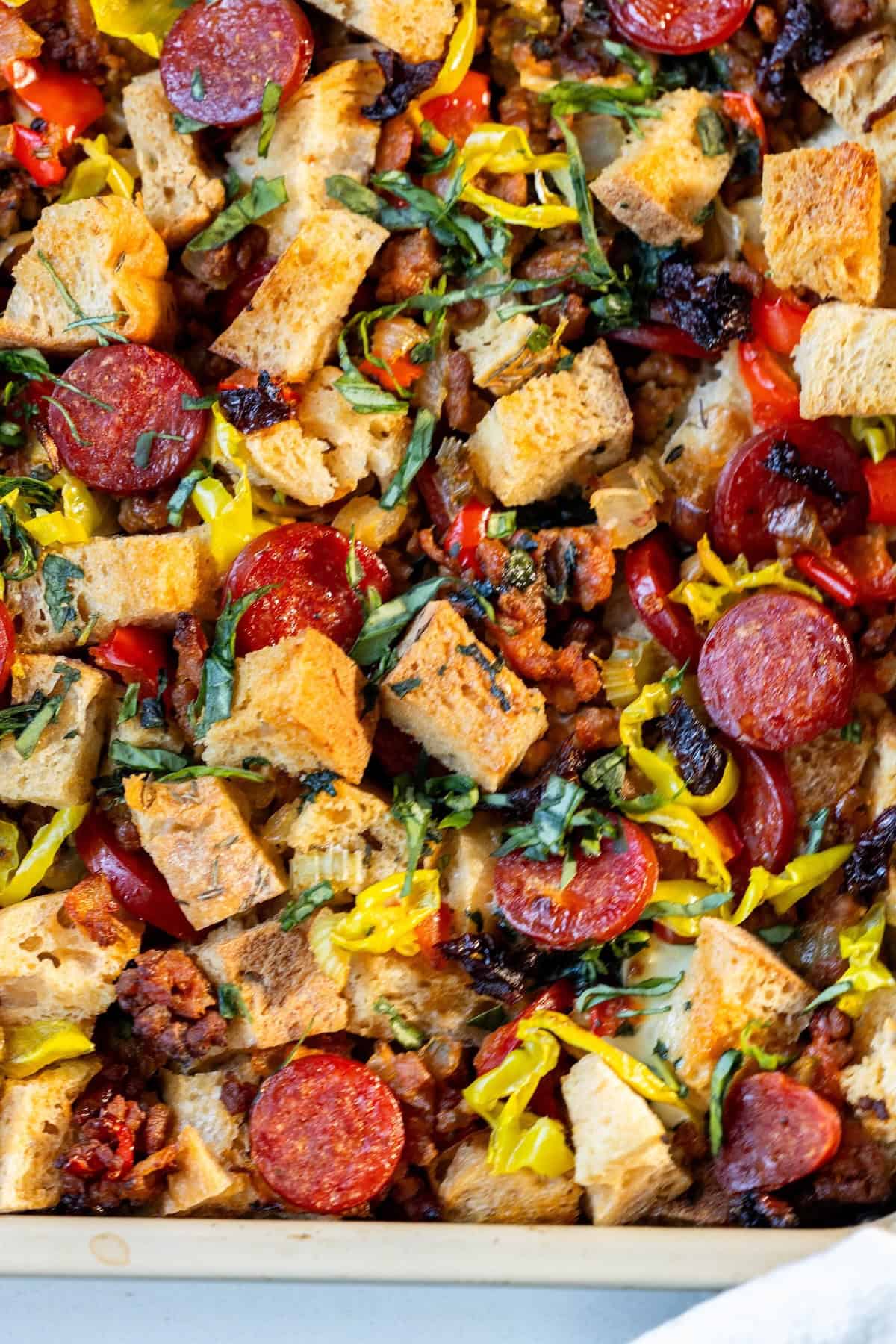 A close-up of a baked dish featuring cubed bread, sliced pepperoni, chopped herbs, banana peppers, and bits of sausage—perfect for those seeking creative pepperoni stuffing or unique pepperoni recipes.