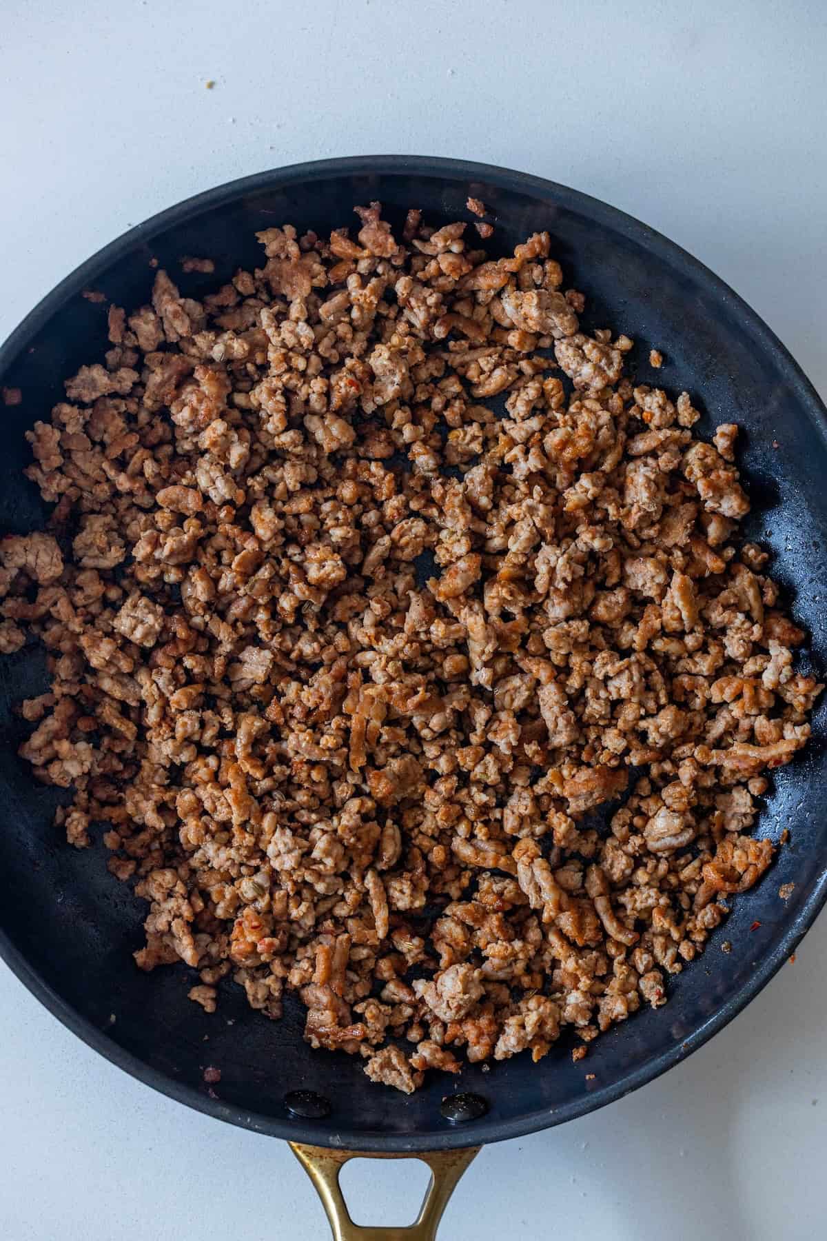 Cooked ground meat and pepperoni in a black skillet on a white surface.