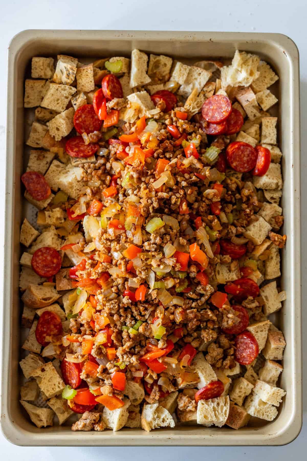 A baking tray filled with cubed bread, sliced pepperoni, and a savory mixture of cooked ground meat, diced vegetables, and seasonings creates a delicious Pepperoni Stuffing.