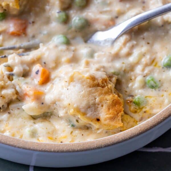 Close-up of a creamy biscuit casserole filled with chicken, vegetables, peas, and carrots, topped with biscuits—perfect for using leftover turkey—in a bowl with a spoon.