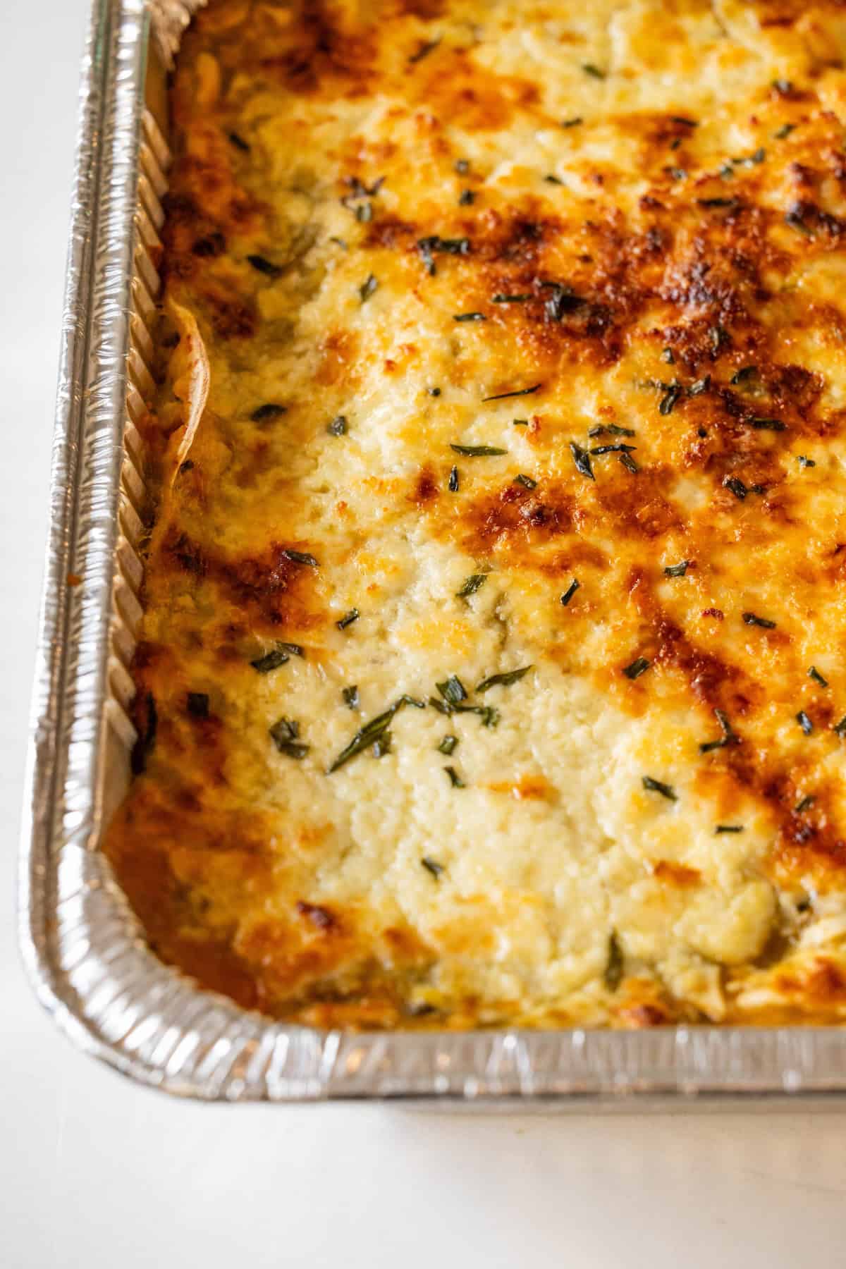A close-up of a cheesy enchilada pie casserole, topped with herbs and baked in a disposable aluminum tray—perfect for using up leftover turkey.