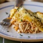 Close-up of a serving of cheesy enchilada pie on a white plate with a fork, garnished with chopped herbs—perfect inspiration for leftover turkey recipes.