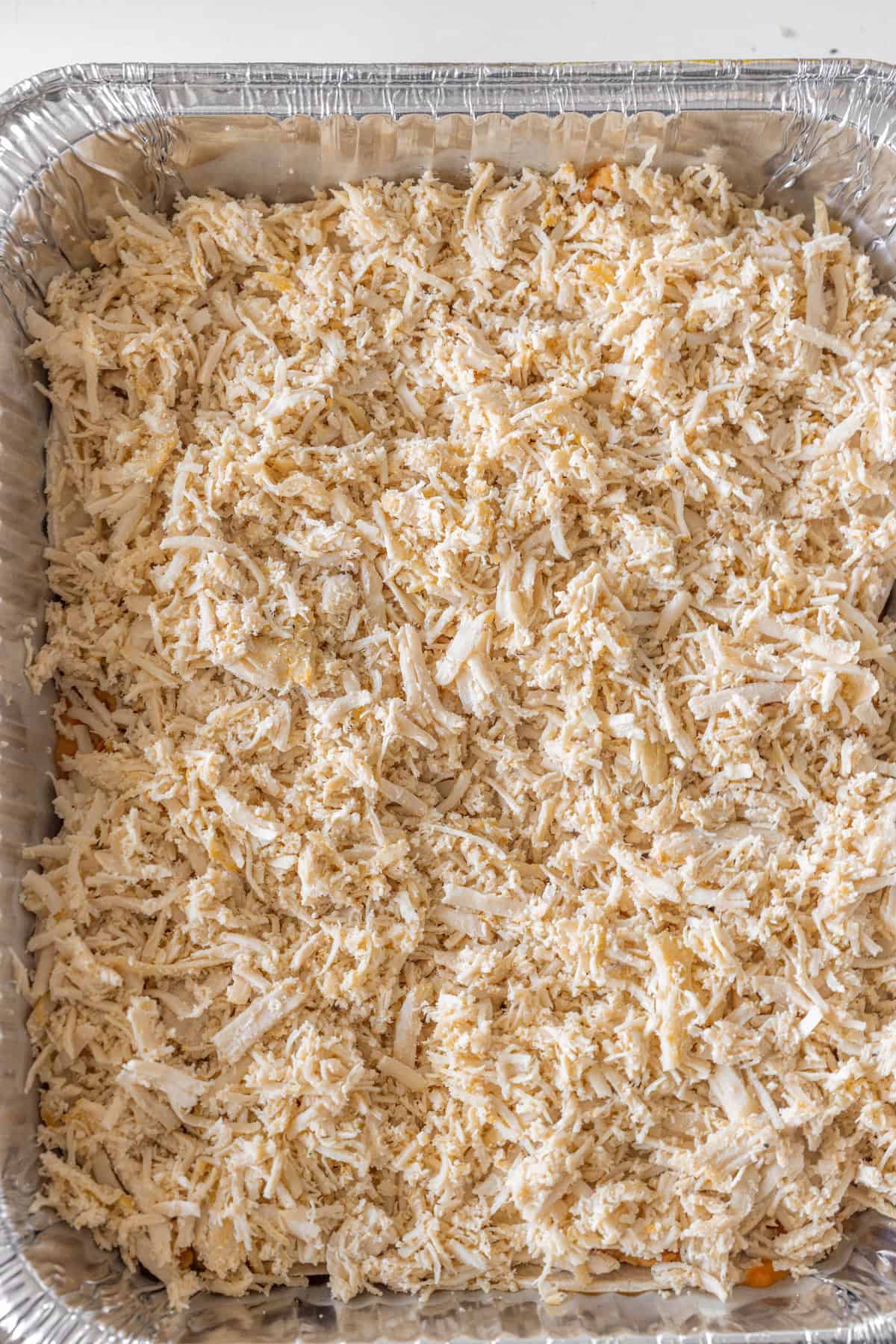 Aluminum tray filled with a layer of shredded cooked chicken, perfect as a base for Enchilada Pie or to swap in for Leftover Turkey in your favorite enchilada recipes.