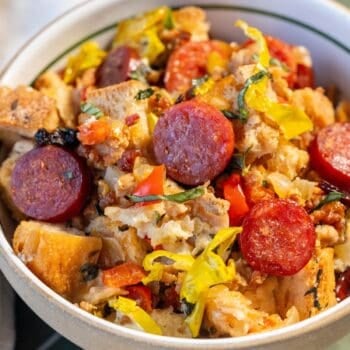A bowl filled with bread pieces, sliced pepperoni, chopped peppers, and herbs, mixed together in a savory stuffing dish.