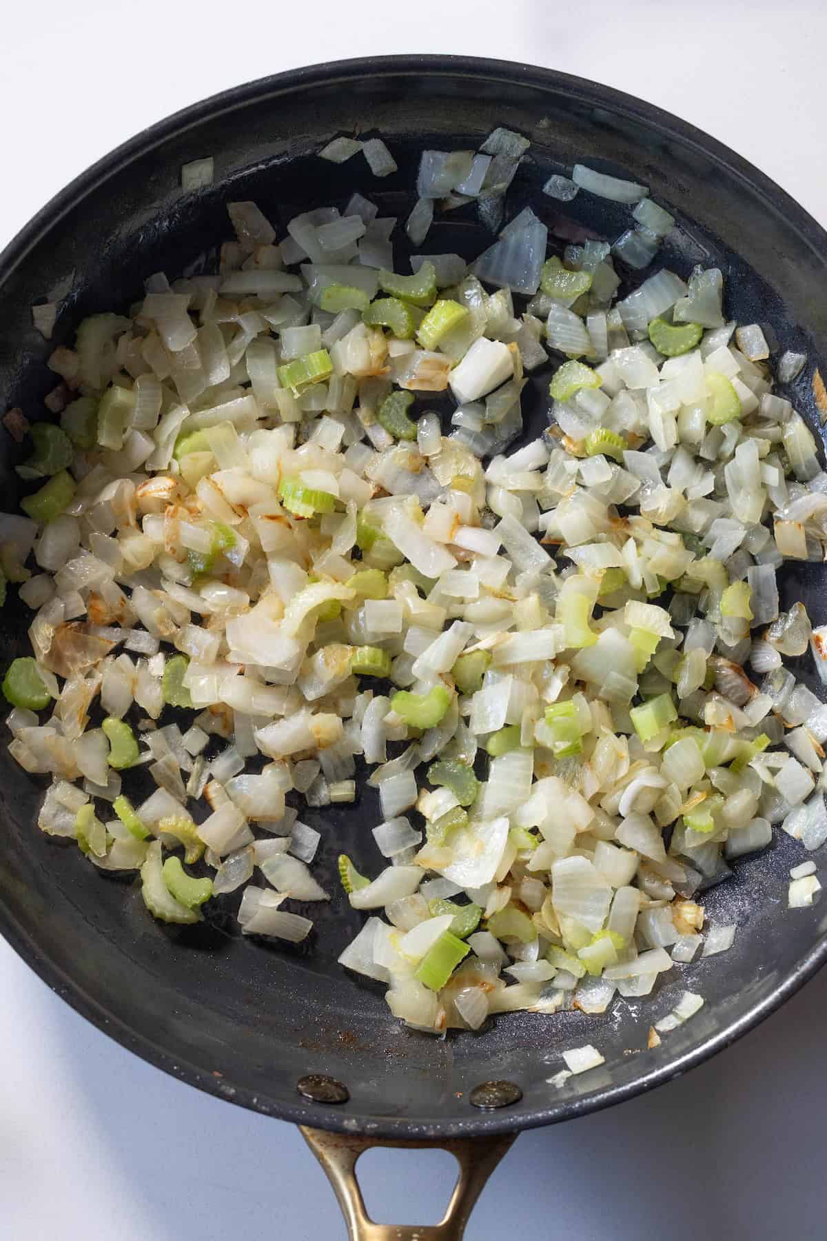 Diced onions and celery being sautéed in a black skillet, showing browning and softening—perfect as a flavor base for savory Kielbasa stuffing.