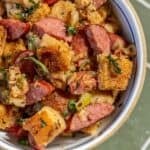 A bowl of sausage and bread stuffing with herbs and chopped vegetables, featuring browned bread cubes and hearty slices of Polish Kielbasa.