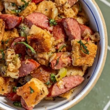 A bowl of sausage and bread stuffing with herbs and chopped vegetables, featuring browned bread cubes and hearty slices of Polish Kielbasa.