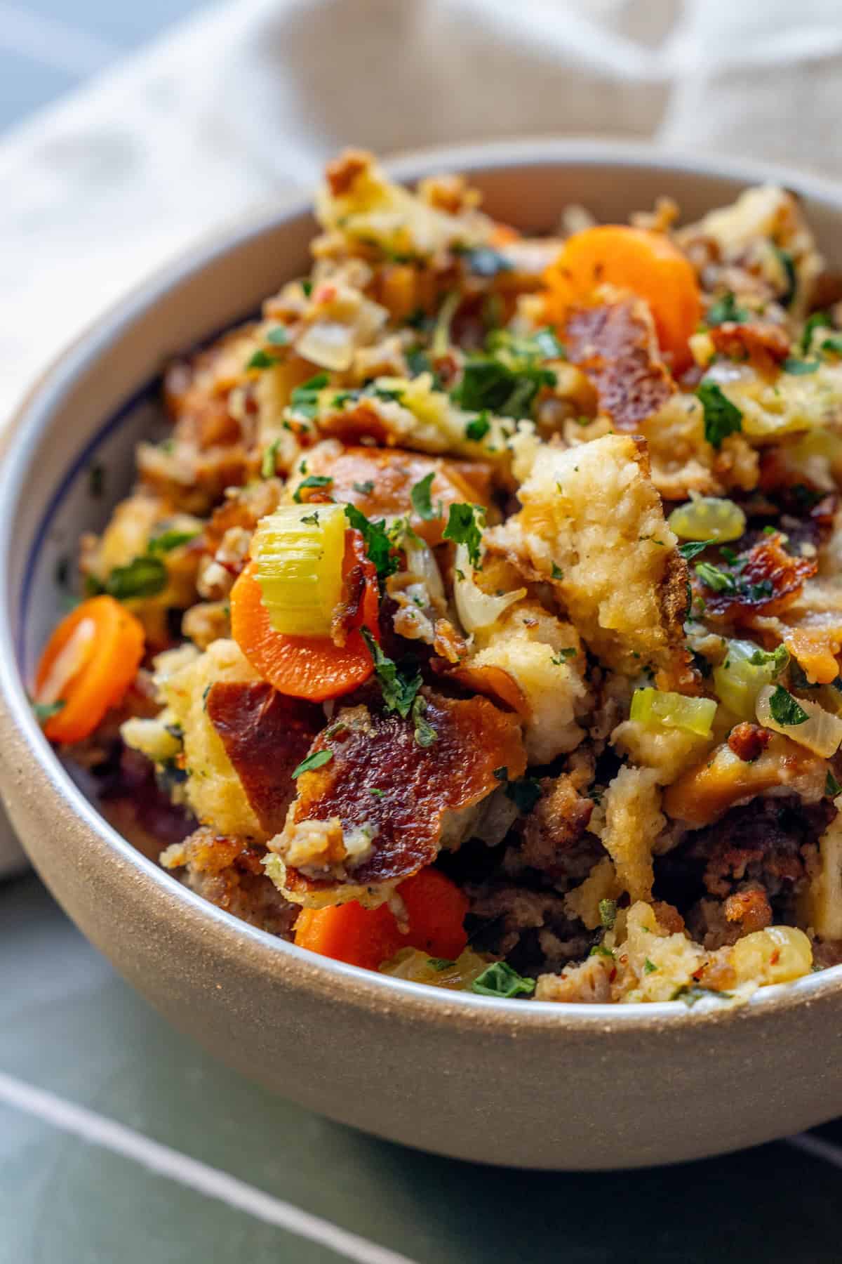 A bowl filled with pretzel sausage stuffing mixed with carrots, celery, herbs, and crispy bacon pieces.