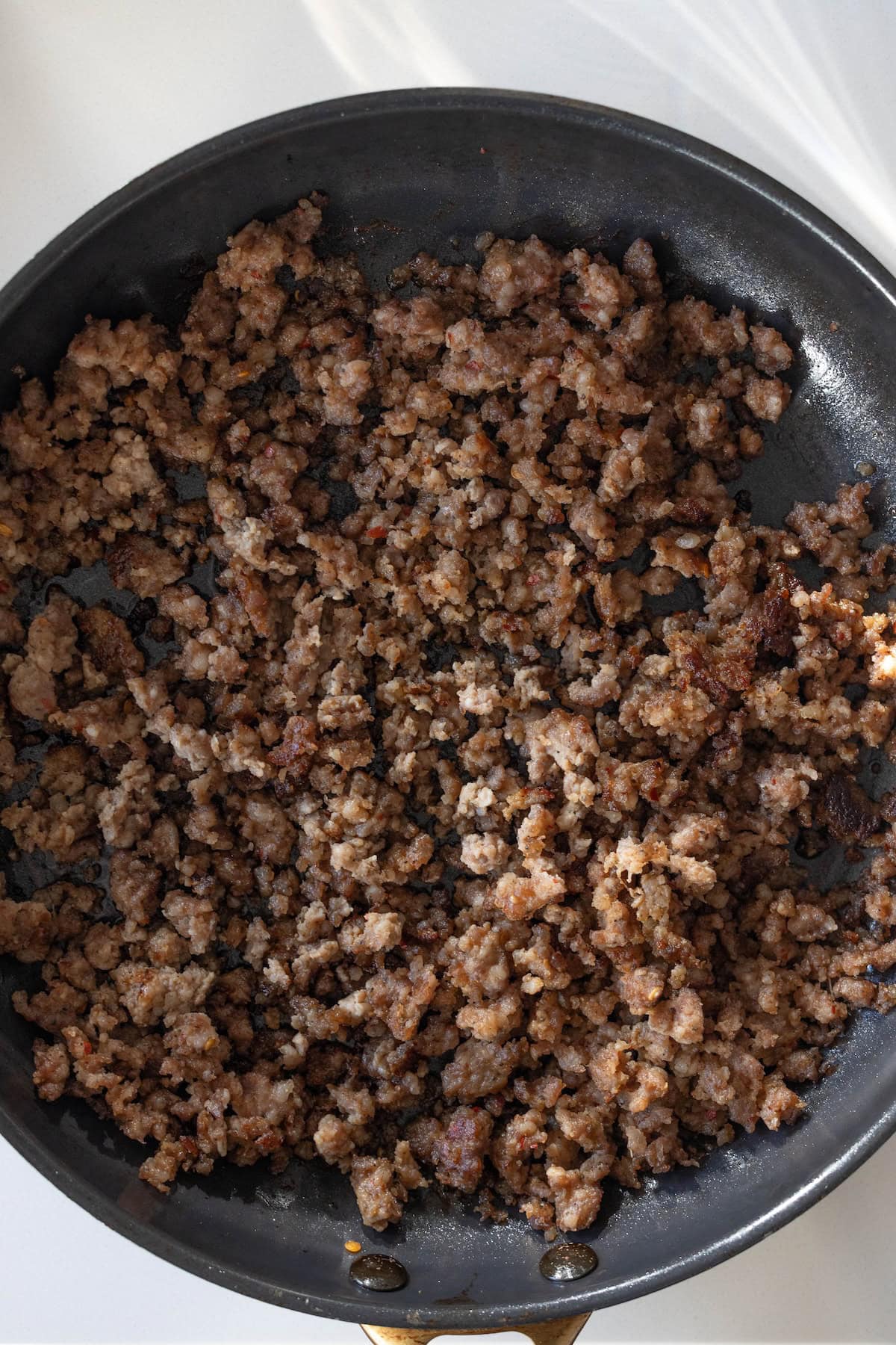 Cooked ground sausage in a black skillet, browned and crumbled into small pieces—perfect for adding to your favorite pretzel sausage stuffing.