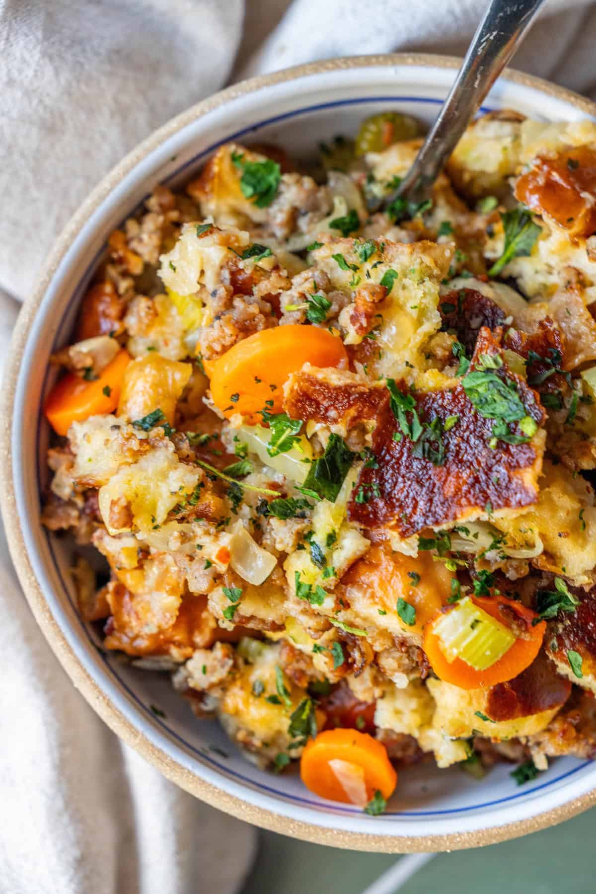 A bowl of pretzel sausage stuffing with chunks of bread, sliced carrots, celery, herbs, and browned crispy edges, served with a spoon in the bowl.