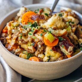 A bowl of sausage stuffing with bread cubes, sliced carrots, celery, herbs, and sausage, garnished with chopped parsley.