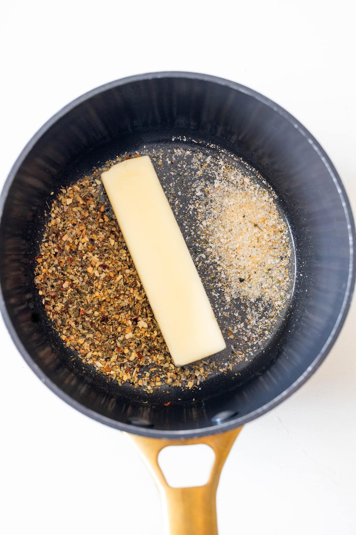 A stick of butter, Italian seasoning, and garlic powder melt in a black saucepan with a wooden handle—perfect for elevating your Best Roast Pork or any Rack of Pork Recipe.