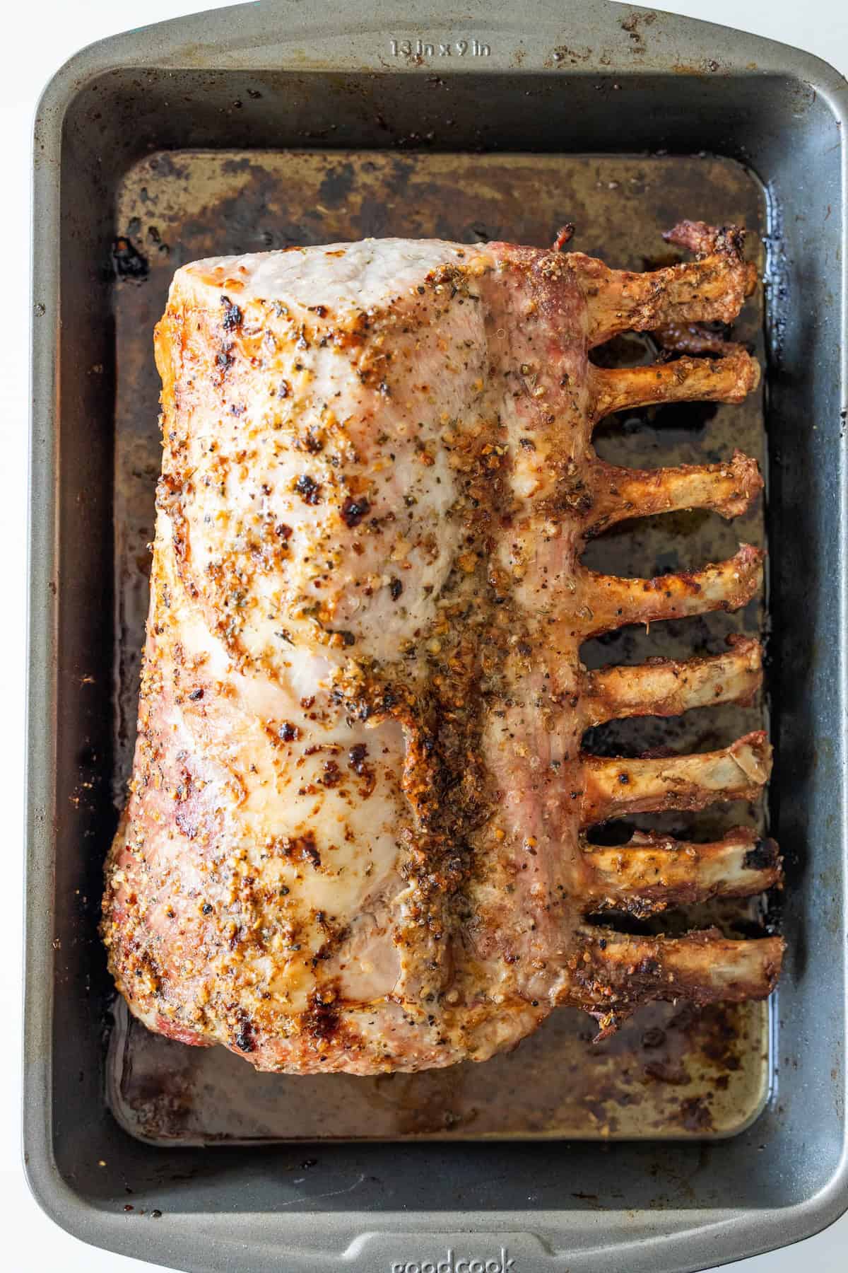 A Roasted Rack of Pork with a seasoned crust rests in a rectangular metal roasting pan, promising the flavors of the best roasted pork.
