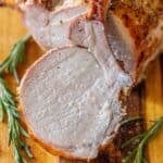 A roasted rack of pork, sliced to reveal its juicy interior, is displayed on a wooden board with fresh rosemary sprigs—a true showcase of the best roasted pork.