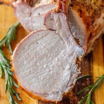A roasted rack of pork, sliced to reveal its juicy interior, is displayed on a wooden board with fresh rosemary sprigs—a true showcase of the best roasted pork.