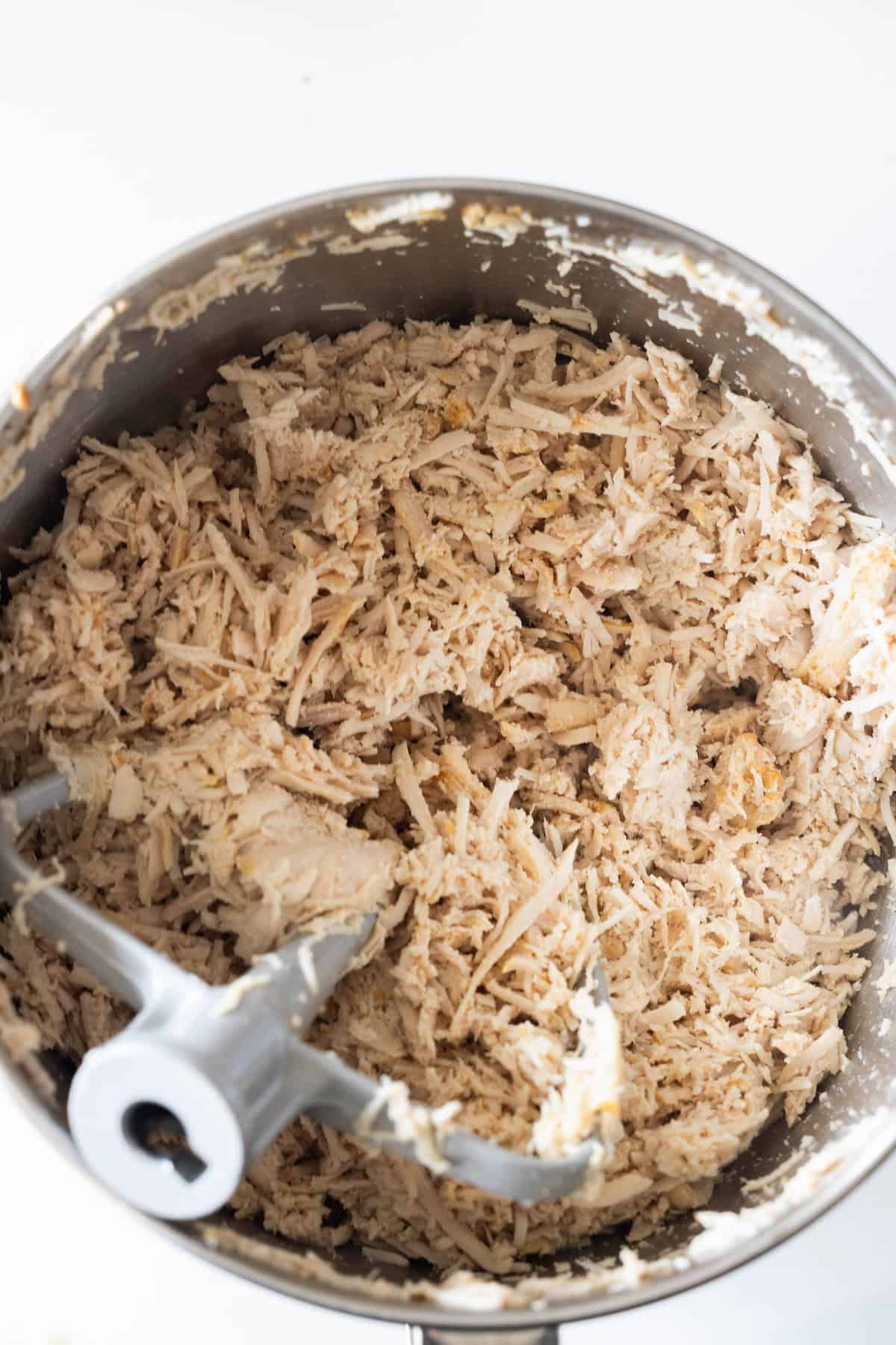 Shredded cooked turkey breast in a metal mixing bowl with a paddle attachment—perfect for recipes using slow cooker shredded turkey.