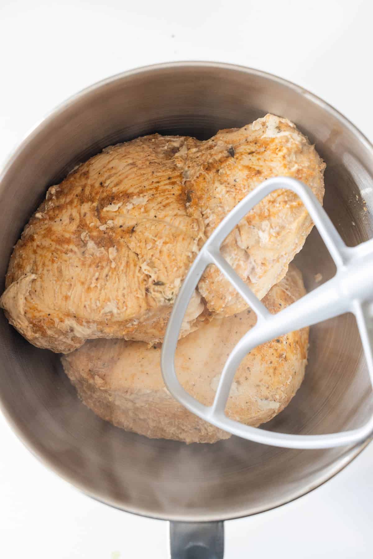 Three cooked turkey breasts in a mixing bowl with a paddle attachment, ready for shredding—perfect for making shredded turkey breast similar to what you’d get from a slow cooker.
