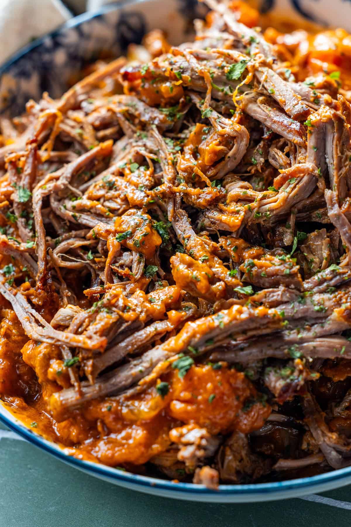 Close-up of shredded beef covered in a rich, red tomato soup pot roast sauce and garnished with chopped herbs, served in a bowl.