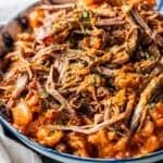 Shredded beef in a rich, orange-red tomato soup pot roast sauce garnished with chopped herbs, served in a shallow bowl.