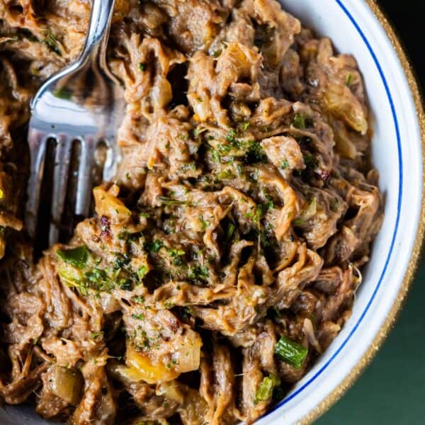 Close-up of shredded Onion Soup Pot Roast mixed with vegetables and herbs in a bowl, with a fork partially visible.