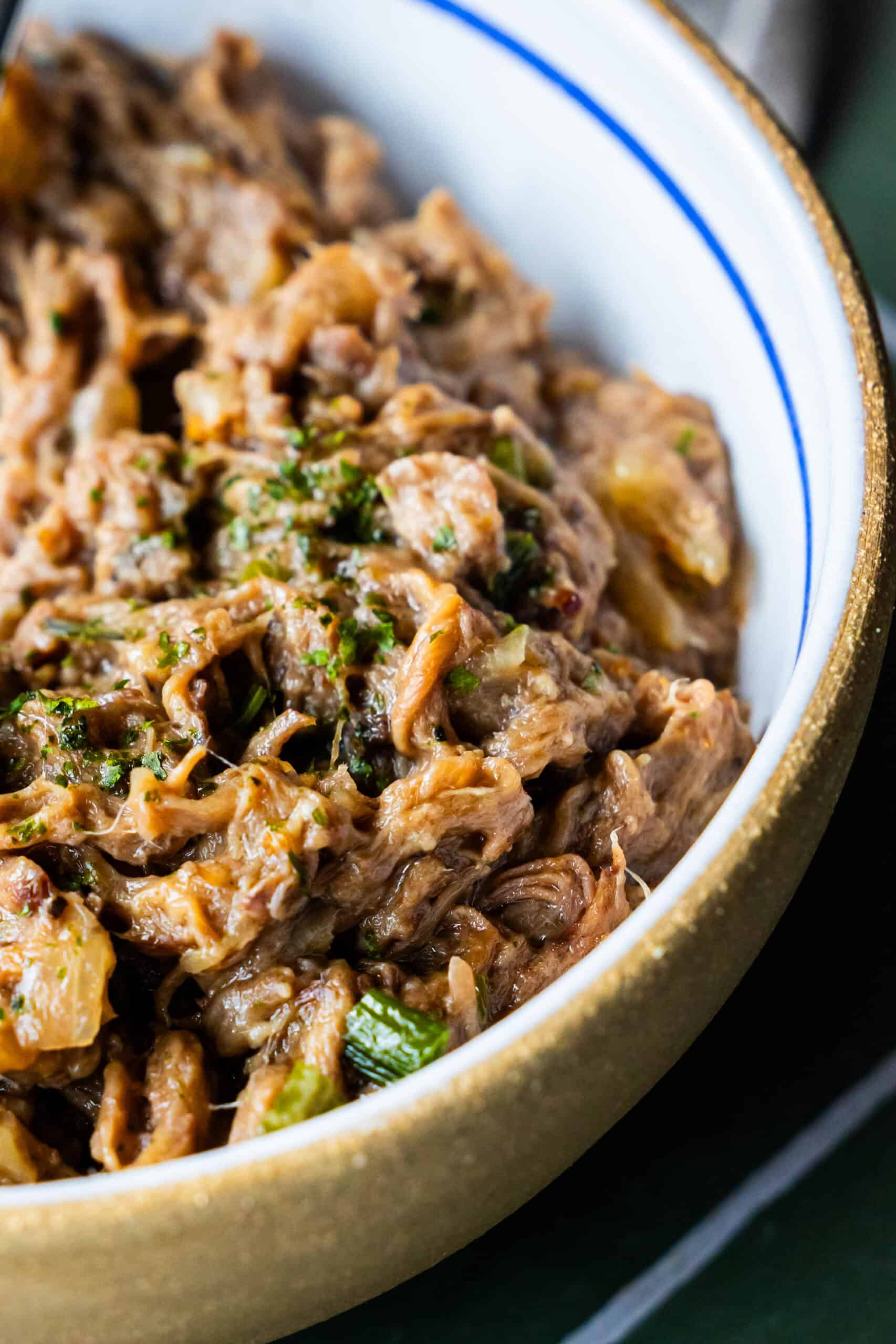 A close-up of shredded beef mixed with vegetables in a white bowl with a gold rim, showcasing the savory richness of an Onion Soup Pot Roast.