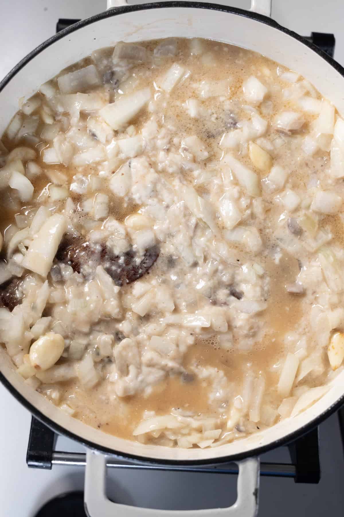 A pot of savory Onion Soup simmers on the stovetop with chopped onions, rice, garlic, and tender pieces of meat in a light broth.